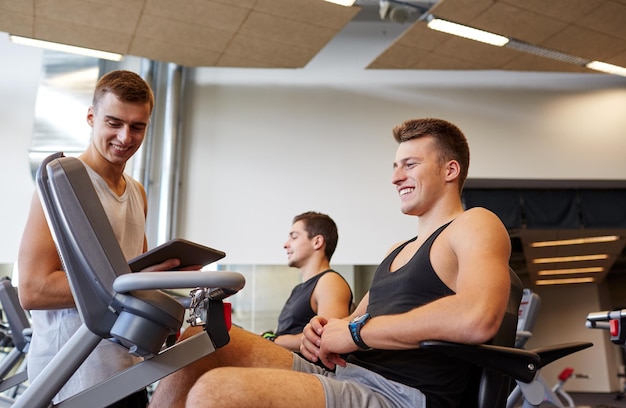 deporte, fitness, equipo, tecnología y concepto de personas - hombres con tablet pc haciendo ejercicio en una máquina de gimnasio