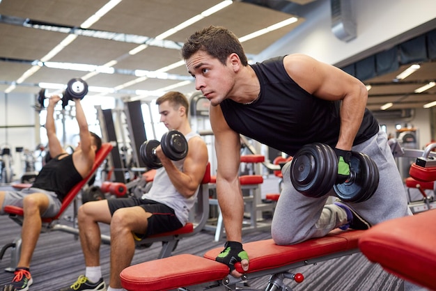 deporte, fitness, estilo de vida y concepto de personas - grupo de hombres flexionando músculos con pesas en el gimnasio