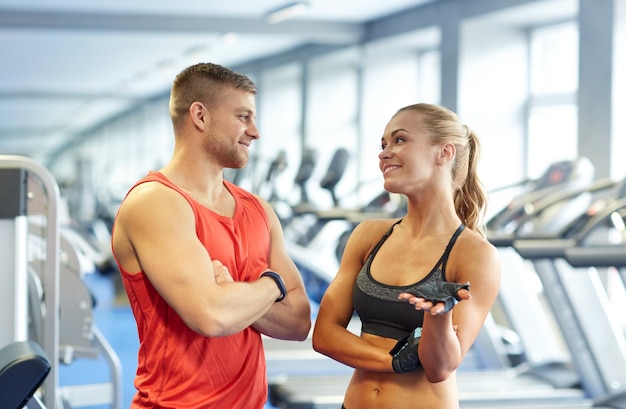 deporte, fitness, estilo de vida y concepto de personas - hombre y mujer sonrientes hablando en el gimnasio