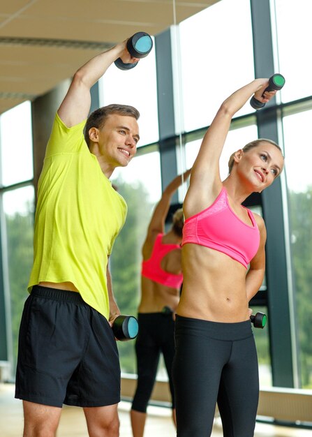 deporte, fitness, estilo de vida y concepto de personas - hombre y mujer sonrientes con pesas haciendo ejercicio en el gimnasio