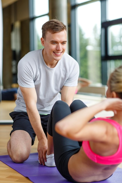 deporte, fitness, estilo de vida y concepto de personas - mujer sonriente con entrenador personal masculino haciendo ejercicio en el gimnasio