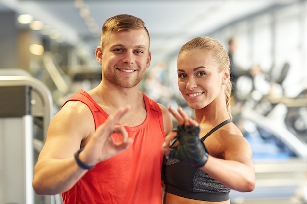 deporte, fitness, estilo de vida, gesto y concepto de la gente - hombre y mujer sonrientes mostrando el signo de la mano en el gimnasio