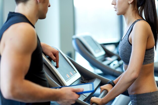 deporte, fitness, estilo de vida, tecnología y concepto de personas - cierre de mujer con entrenador trabajando en cinta de correr en el gimnasio