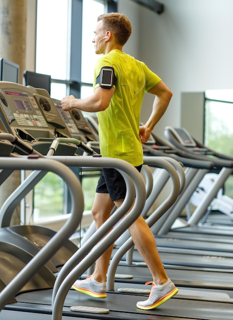 deporte, fitness, estilo de vida, tecnología y concepto de personas - hombre con smartphone y auriculares haciendo ejercicio en la cinta de correr en el gimnasio