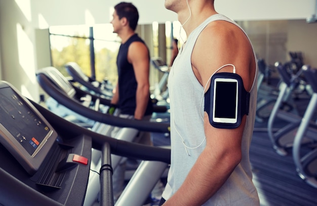 deporte, fitness, estilo de vida, tecnología y concepto de personas - hombre con smartphone y auriculares haciendo ejercicio y escuchando música en la cinta de correr en el gimnasio