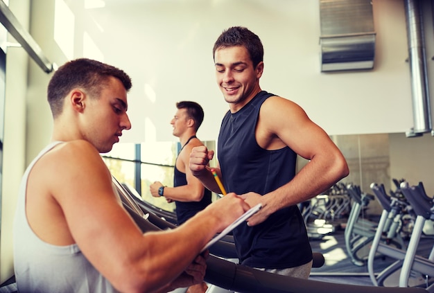 deporte, fitness, estilo de vida, tecnología y concepto de personas - hombres con entrenador personal haciendo ejercicio en la cinta de correr en el gimnasio