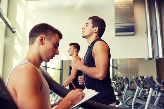 deporte, fitness, estilo de vida, tecnología y concepto de personas - hombres con entrenador personal haciendo ejercicio en la cinta de correr en el gimnasio