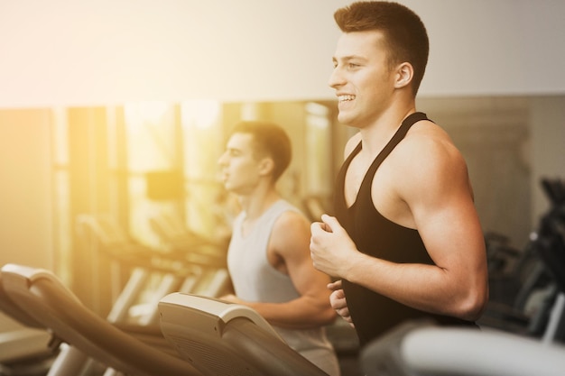 deporte, fitness, estilo de vida, tecnología y concepto de personas - hombres sonrientes haciendo ejercicio en la cinta de correr en el gimnasio