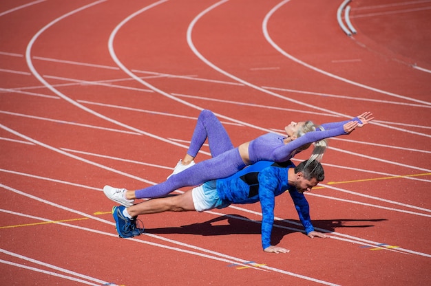 Deporte fitness hombre y mujer entrenando juntos parados en la tabla y hacer empuje hacia arriba en la pista de carreras del estadio al aire libre con ropa deportiva, entrenamiento deportivo.