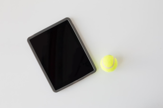 deporte, fitness, juego, equipo deportivo y concepto de tecnología - cierre de pelota de tenis y tablet pc con pantalla negra en blanco sobre fondo blanco desde arriba