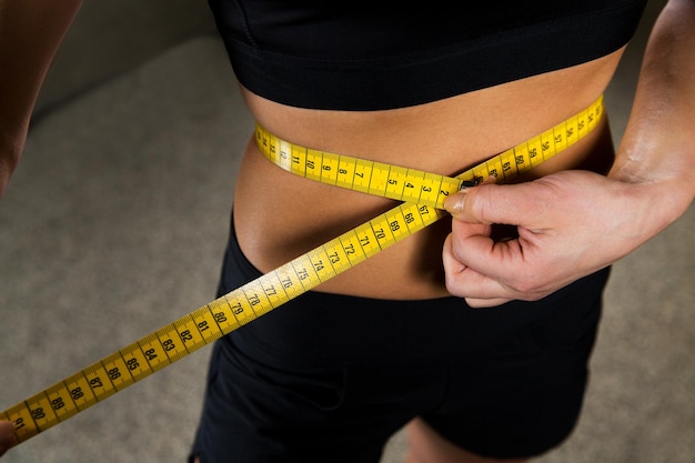 deporte, fitness, pérdida de peso, dieta y concepto de personas: cierre de una mujer que mide el tamaño de la cintura con cinta en el gimnasio