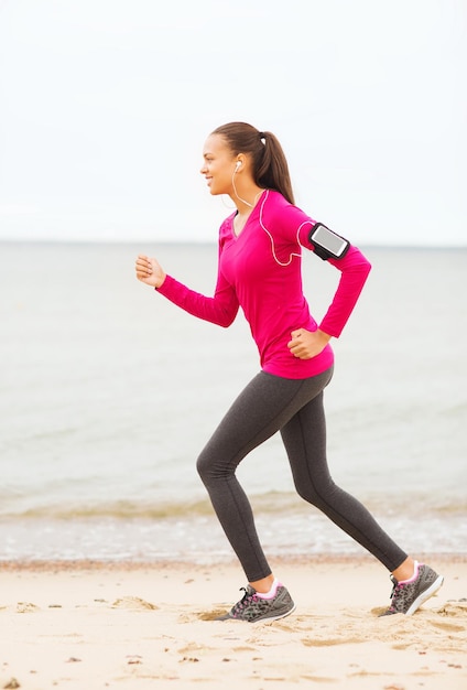 deporte, fitness, salud, tecnología y concepto de personas - joven afroamericana sonriente corriendo con smartphone y auriculares al aire libre