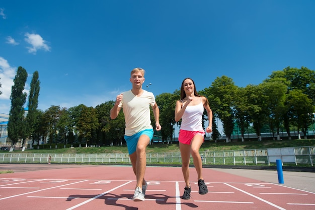 Deporte y fitness saludable. Pareja corriendo en pista de arena. Hombre y mujer al aire libre soleado en el cielo azul. Entrenador y formador en el entrenamiento. Corredor en competencia y éxito futuro.