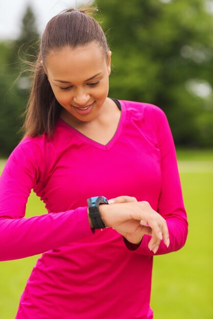 deporte, fitness, tecnología, salud y concepto de personas - mujer joven sonriente con reloj de frecuencia cardíaca al aire libre