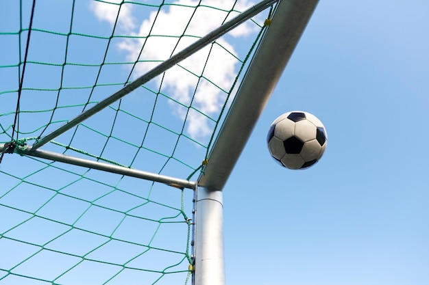 deporte, fútbol y juego - pelota volando hacia la portería de fútbol sobre el cielo azul