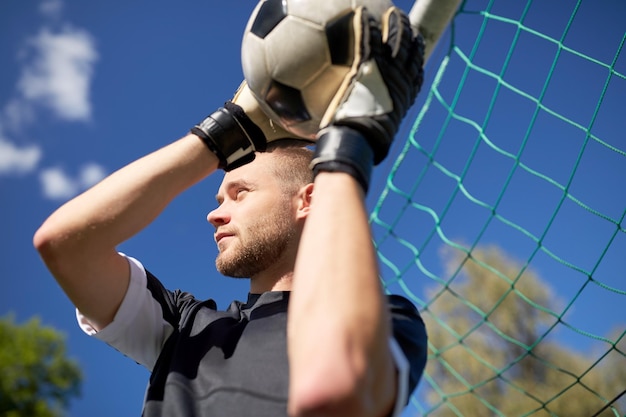 deporte y gente - jugador de fútbol o portero con pelota en el gol de fútbol en el campo