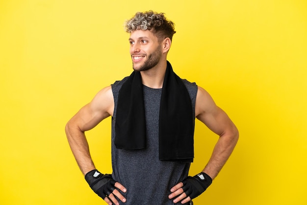 Deporte hombre caucásico aislado sobre fondo amarillo posando con los brazos en la cadera y sonriendo