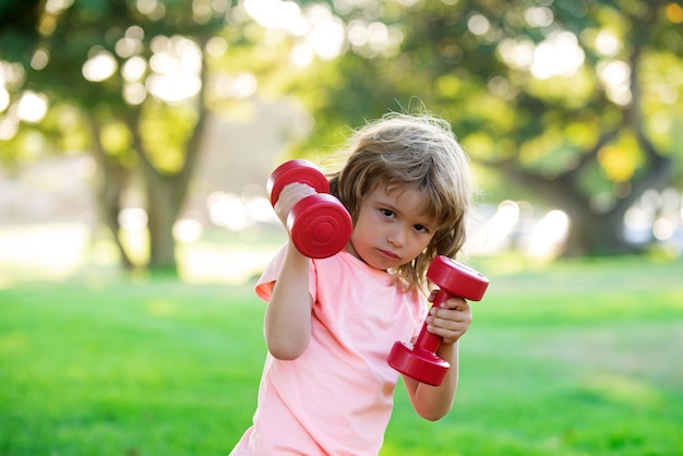 Deporte infantil. Niño haciendo ejercicio en el parque. Estilo de vida activo y saludable. Niño deportivo con fuertes músculos bíceps haciendo ejercicio con mancuernas.