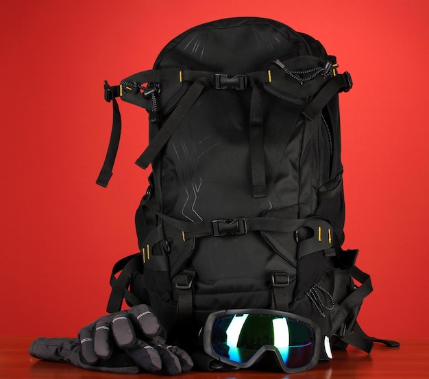 Deporte de invierno gafas casco y guantes mochila sobre fondo rojo.