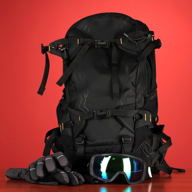 Deporte de invierno gafas casco y guantes mochila sobre fondo rojo.