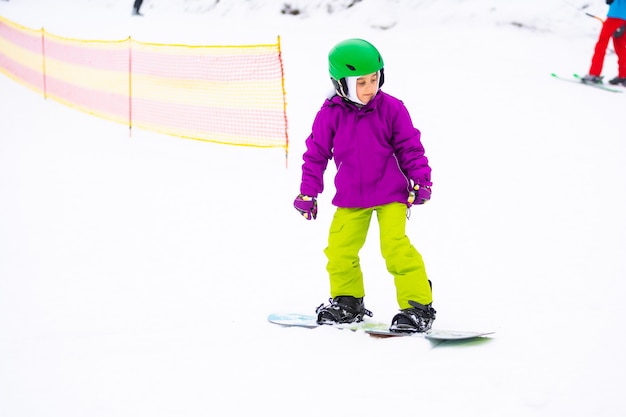 Deporte de invierno de snowboard. niña aprendiendo a hacer snowboard, vistiendo ropa abrigada de invierno. Fondo de invierno.