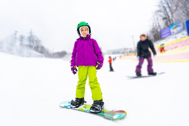 Deporte de invierno de snowboard. niña aprendiendo a hacer snowboard, vistiendo ropa abrigada de invierno. Fondo de invierno.