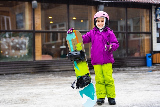 Deporte de invierno de snowboard. niña aprendiendo a hacer snowboard, vistiendo ropa abrigada de invierno. Fondo de invierno.