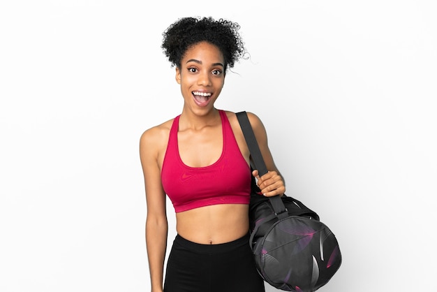 Deporte joven mujer afroamericana con bolsa de deporte aislado sobre fondo azul con expresión facial sorpresa