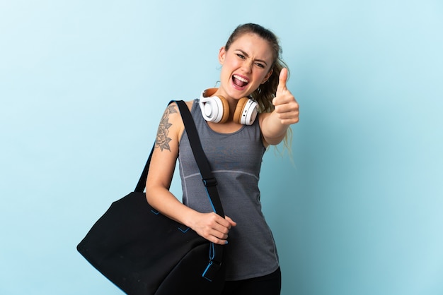 Deporte joven mujer brasileña con bolsa de deporte aislado sobre fondo azul con los pulgares hacia arriba porque algo bueno ha sucedido