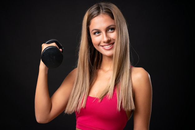 Deporte joven mujer rubia haciendo pesas sobre fondo negro aislado