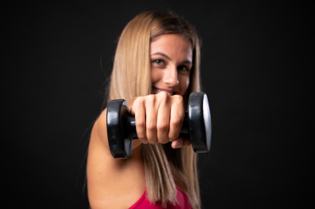 Deporte joven mujer rubia haciendo pesas sobre fondo negro aislado