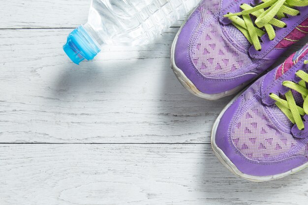 El deporte plano pone los zapatos y la botella púrpuras de agua en el fondo de madera blanco.