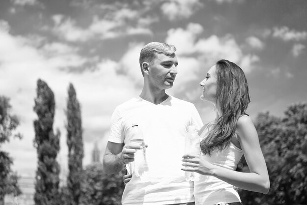 Deporte y salud Mujer y hombre beben agua de la botella Actividad y energía de verano Chica y chico soleado al aire libre Pareja de entrenador relajarse después del entrenamiento