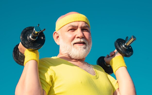 Deporte senior hombre ejercicio con mancuerna estar en movimiento abuelo deportista retrato en blue sky ba