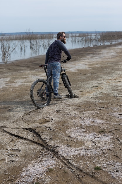 Deportes barbudo brutal en una bicicleta de montaña moderna. Un ciclista en un lugar desierto de sal junto al lago.