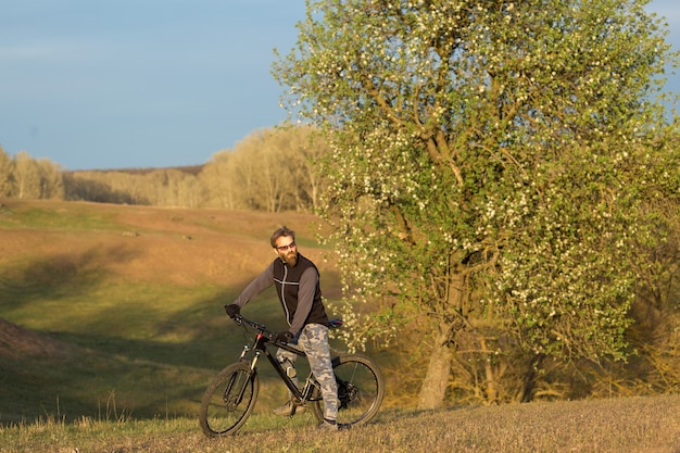 Deportes barbudo brutal en una bicicleta de montaña moderna. Ciclista en las verdes colinas en primavera.
