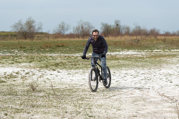 Deportes brutal chico barbudo en una bicicleta de montaña moderna Un ciclista en un lugar desierto de sal junto al lago