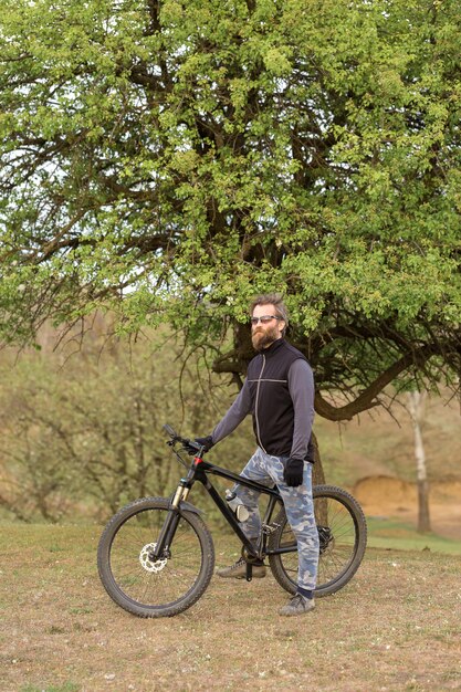 Deportes brutal chico barbudo en una bicicleta de montaña moderna Ciclista en las verdes colinas en la primavera