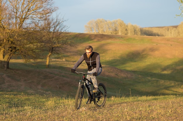 Deportes brutal chico barbudo en una bicicleta de montaña moderna Ciclista en las verdes colinas en la primavera