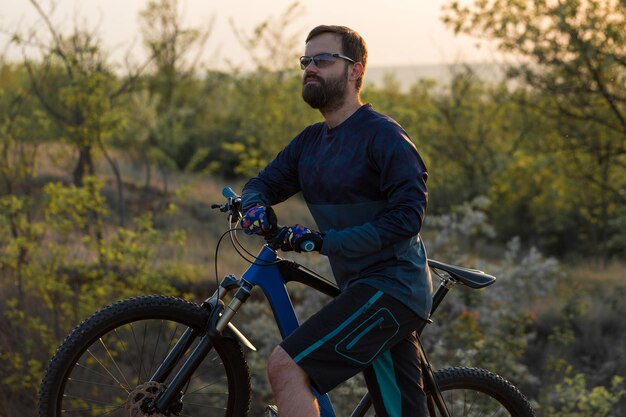 Deportes brutal chico barbudo en una bicicleta de montaña moderna Ciclista en las verdes colinas en la primavera