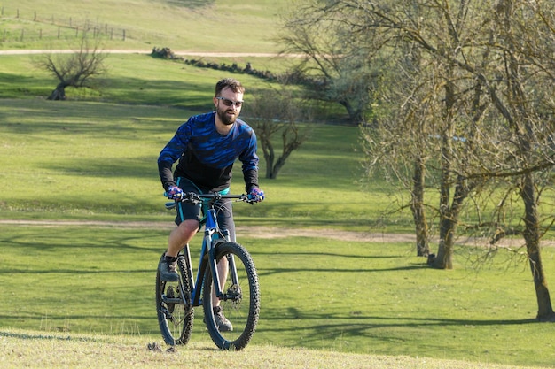 Deportes brutal chico barbudo en una bicicleta de montaña moderna Ciclista en las verdes colinas en la primavera