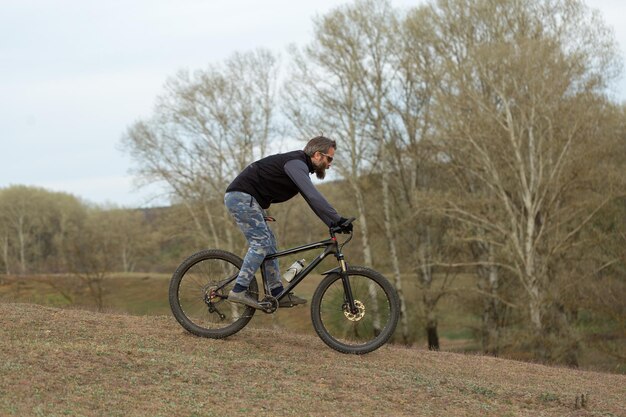 Deportes brutal chico barbudo en una bicicleta de montaña moderna Ciclista en las verdes colinas en la primavera