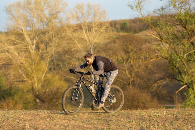 Deportes brutal chico barbudo en una bicicleta de montaña moderna Ciclista en las verdes colinas en la primavera