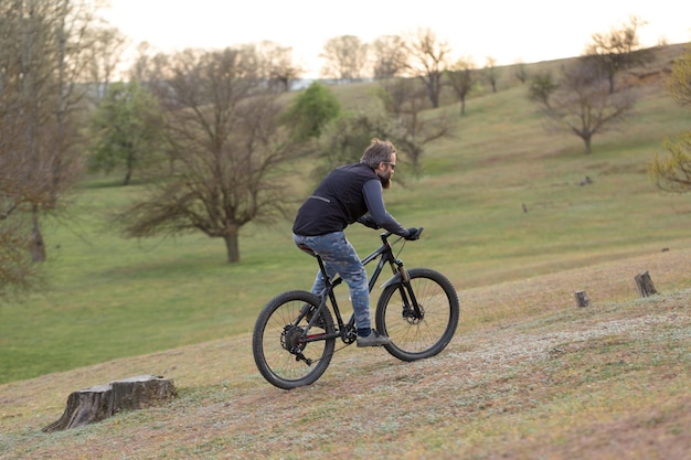 Deportes brutal chico barbudo en una bicicleta de montaña moderna Ciclista en las verdes colinas en la primavera