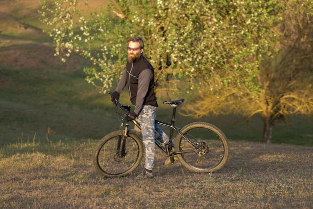 Deportes brutal chico barbudo en una bicicleta de montaña moderna Ciclista en las verdes colinas en la primavera