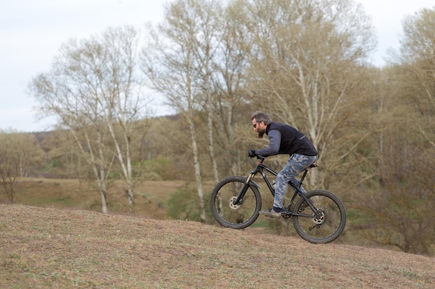 Deportes brutal chico barbudo en una bicicleta de montaña moderna Ciclista en las verdes colinas en la primavera