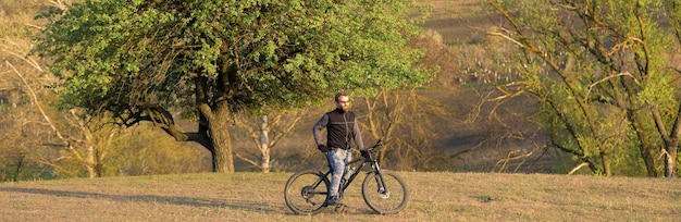 Deportes brutal chico barbudo en una bicicleta de montaña moderna Ciclista en las verdes colinas en la primavera