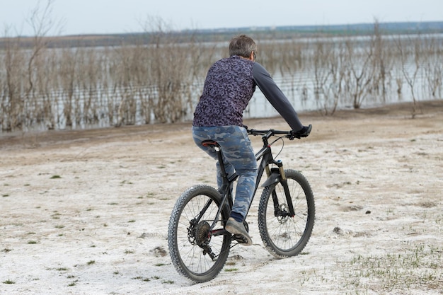 Deportes brutal hombre barbudo en una bicicleta de montaña moderna Un ciclista en un lugar desierto de sal junto al lago
