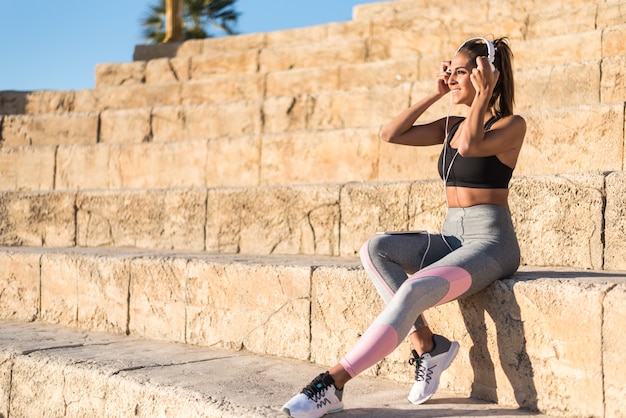 Deportes mujer descansando y escuchando música usando su teléfono móvil en las escaleras