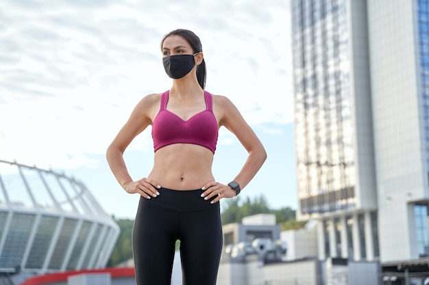 Deportes mujer joven en mascarilla preparándose para un trote en la ciudad. Concepto de estilo de vida saludable